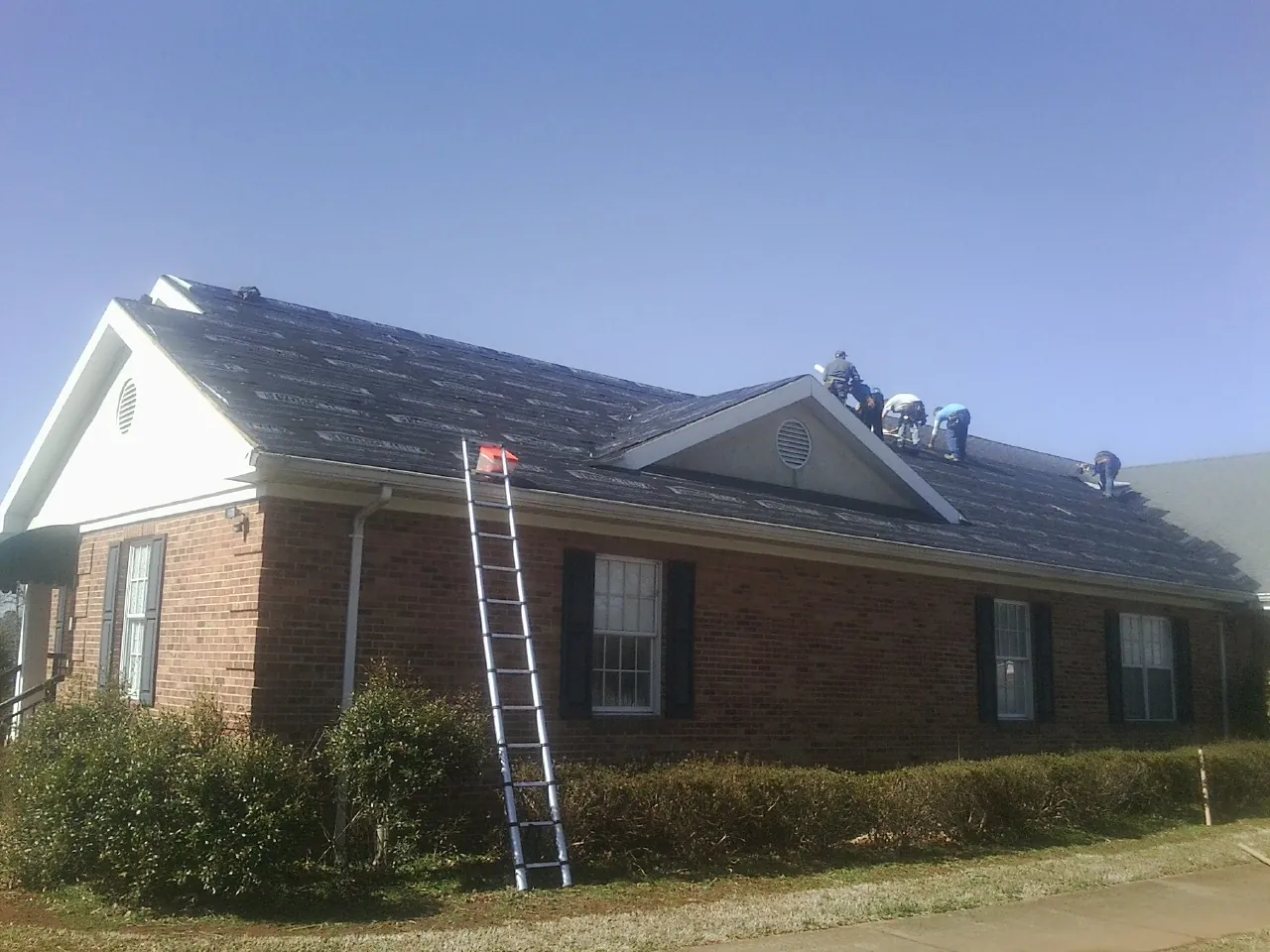 Crew tearing shingles off a brick ranch roof with a ladder set — Metal Roof Repair work by our crew in Callicoon