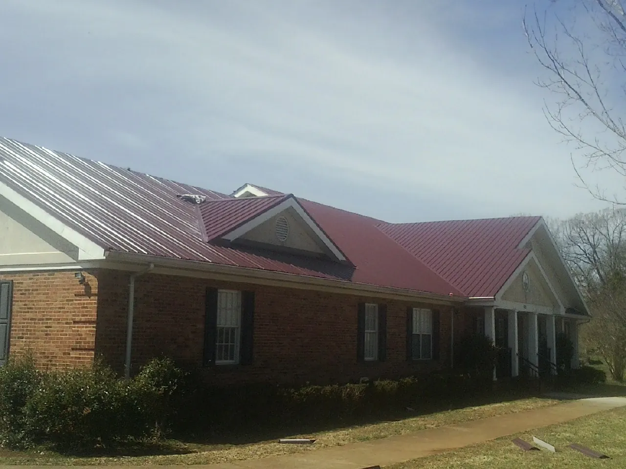 Red metal roof with gabled entries on a long brick building, from a Hail Damage Roof Repair job in Callicoon