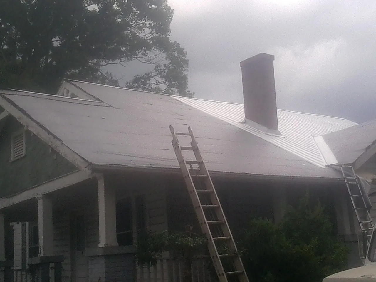 Ladders against a metal roof on an older home with a brick chimney in Callicoon