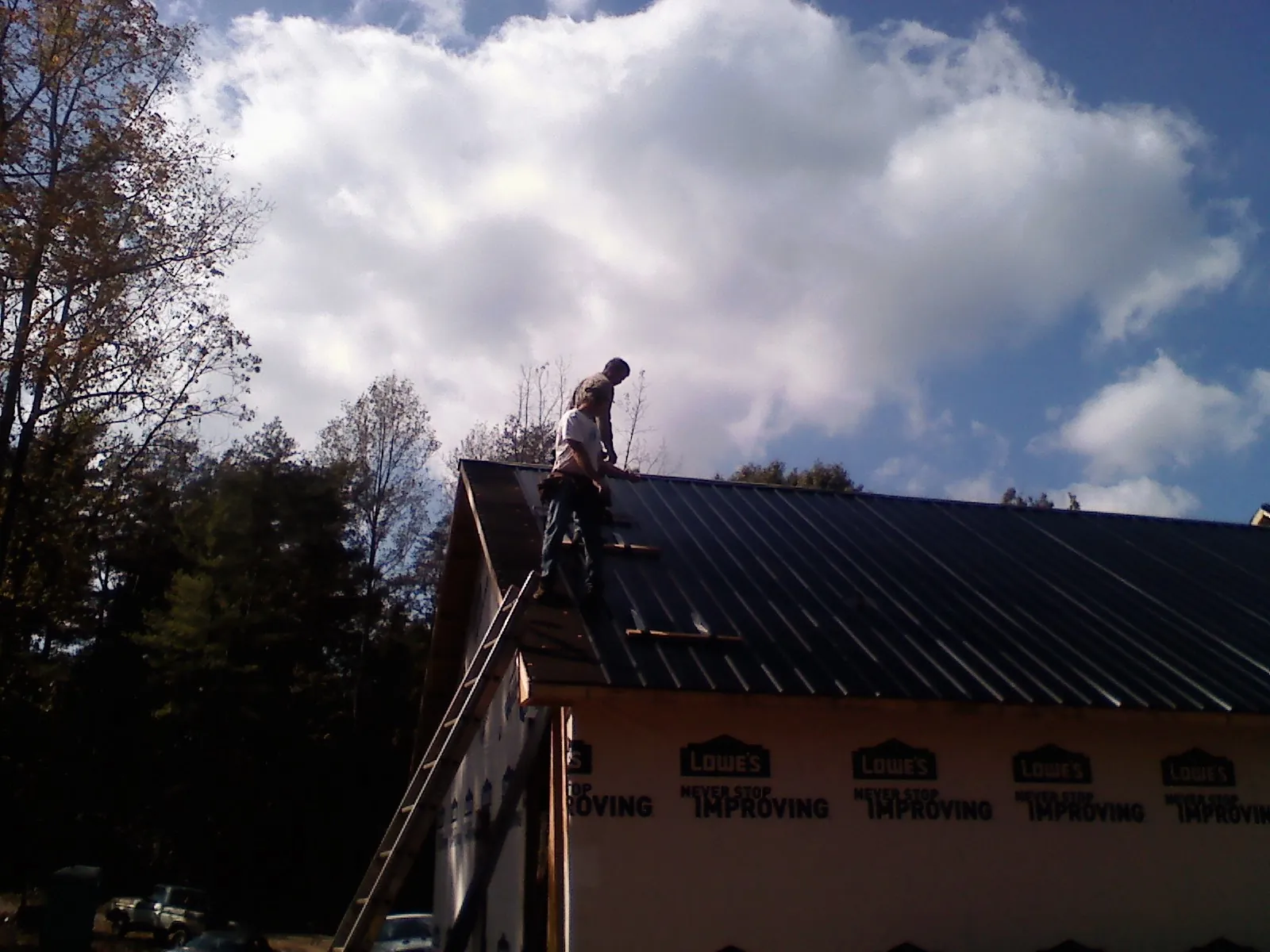 Roofer fastening dark metal panels high against a cloudy sky, from a Roof Inspection job in Callicoon