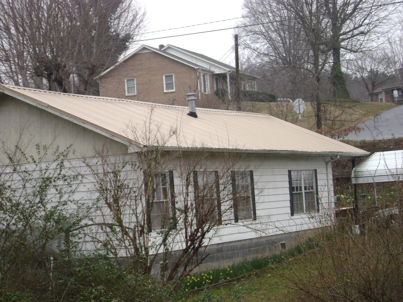 Tan metal roof on a white sided house set into a hillside — Commercial Roofing by Roofing Brothers in Callicoon